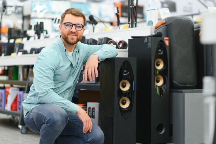 Auf diesem Bild hockt ein Mann neben Lautsprecherboxen.