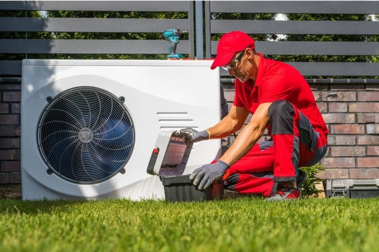 Auf diesem Bild kniet ein Handwerker vor einer Wärmepumpe.