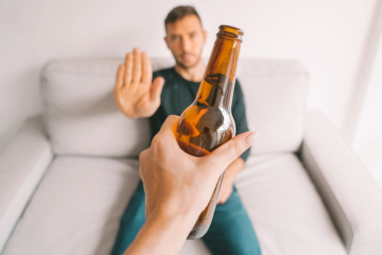 Auf dem Bild ist ein Mann zu sehen, dem eine Bierflasche hingehalten wird, dieser lehnt ab.