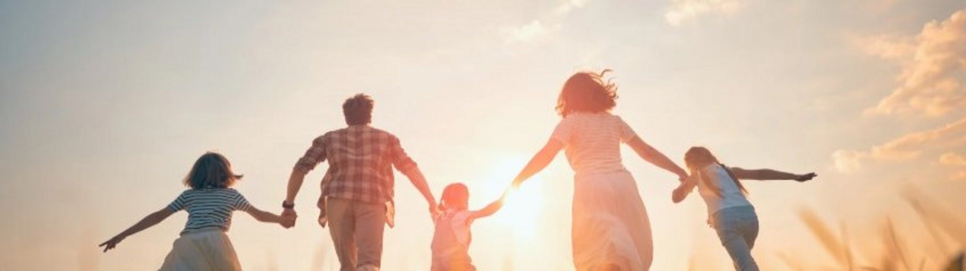 Auf diesem Bild laufen zwei Erwachsene und drei Kinder Hand in Hand in den Sonnenuntergang.