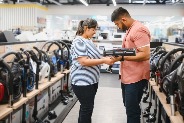 Auf diesem Bild stehen zwei Personen in einem Geschäft mit vielen Staubsaugern.