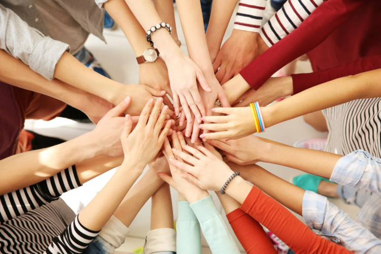 Auf diesem Bild sind viele Personen zu sehen, die in einem Kreis stehen und die Hände in der Mitte aufeinander gelegt haben.