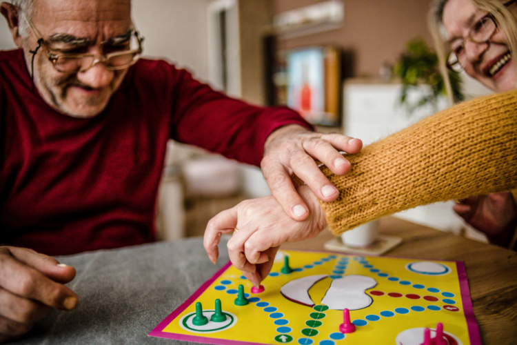 Auf diesem Bild sind zwei ältere Personen zu sehen, die gemeinsam ein Brettspiel spielen.