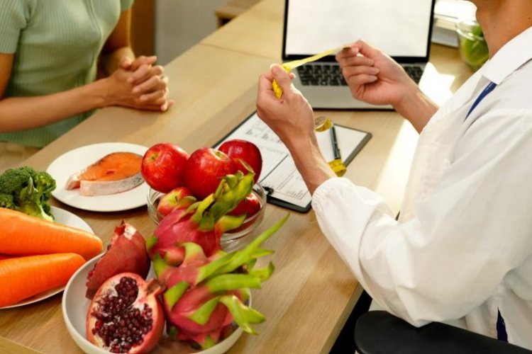 Auf diesem Bild sitzen sich ein Arzt und eine Patientin gegenüber. Auf dem Tisch zwischen ihnen liegen verschiedene gesunde Lebensmittel.