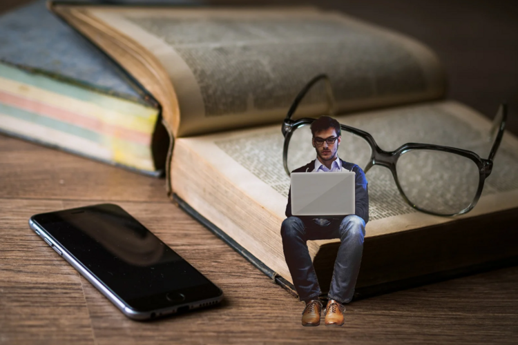 Auf diesem Bild ist eine Person vor einem Laptop zu sehen, die auf einem Buch sitzt.