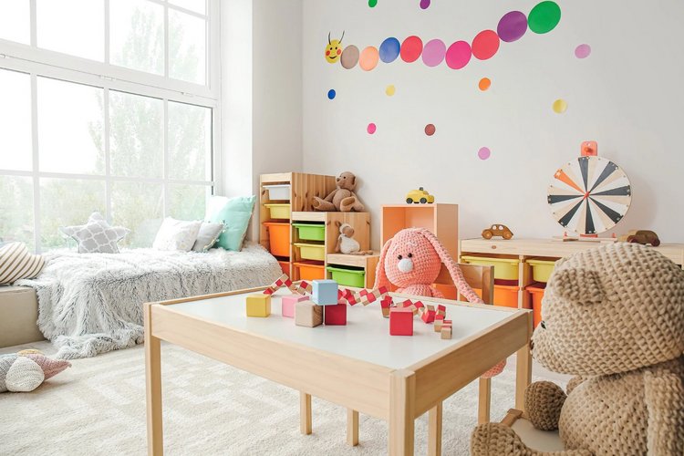 Auf diesem Bild ist ein Zimmer mit Sofa, Tisch und Regalen mit Spielsachen zu sehen. 