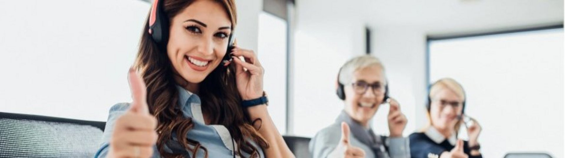 Auf diesen Bild haben drei Frauen Headsets auf und zeigen den hochgestreckten Daumen in die Luft.
